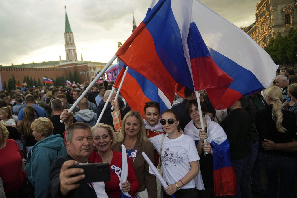 
Cilvēki uzņem pašbildes, vicinot Krievijas nacionālos karogus, Sarkanajā laukumā, lai skatītos koncertu, kas veltīts Krievijas dienai. Maskava, Krievija, 2025. gada 11. jūnijs.
